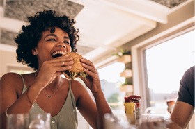 Smiling woman eating burger at restaurant