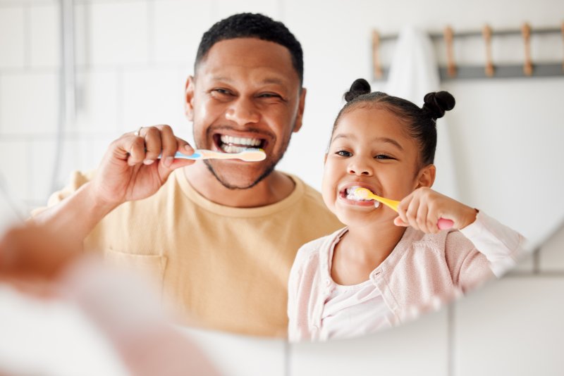 A father and daughter celebrate oral hygiene month by brushing their teeth together